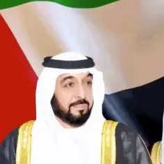 Trzech arabskich przywódców w tradycyjnych strojach, na tle flagi Zjednoczonych Emiratów Arabskich. Jeden z nich, być może najbogatszy szejk na świecie, patrzy wprost.
