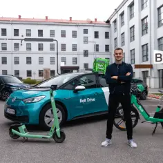 Młody mężczyzna stoi obok zielonego elektrycznego skutera i samochodu Bolt Drive. Czy w Mediolanie jest Bolt? Tak, jest!