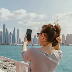 Kobieta robi zdjęcie telefonem na tle Dubaju. Zastanawia się, czy podatek w Dubaju wpłynie na jej wakacje.