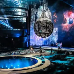 Spektakl w La Perle Dubai: artyści na scenie z basenem, wiszącą kulą i kosmicznym tłem.
