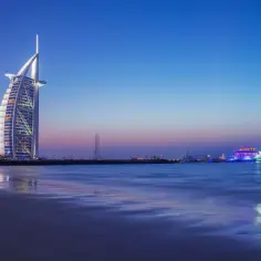Zachód słońca w Dubaju, z luksusowym hotelem Burj Al Arab i oświetloną łodzią. Zastanawiasz się, ile kosztuje wycieczka do Dubaju?