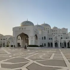 Majestatyczny Qasr Al Watan z białego kamienia, z wieloma kopułami i ozdobnym dziedzińcem, gdzie spacerują ludzie.