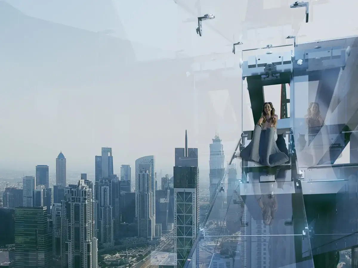Widok z góry na Dubaj, dwie kobiety zjeżdżają po szklanej zjeżdżalni, emocje na twarzach.