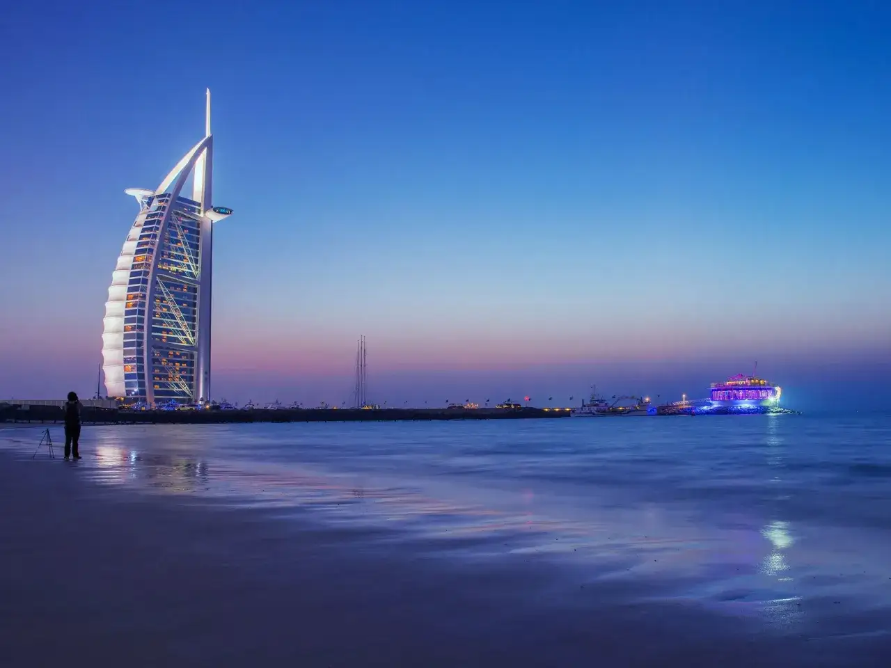 Wieczór w Dubaju, z lśniącym hotelem Burdż al-Arab i kolorową łodzią na morzu. Czy warto jechać do Dubaju? Widok zapiera dech w piersiach!