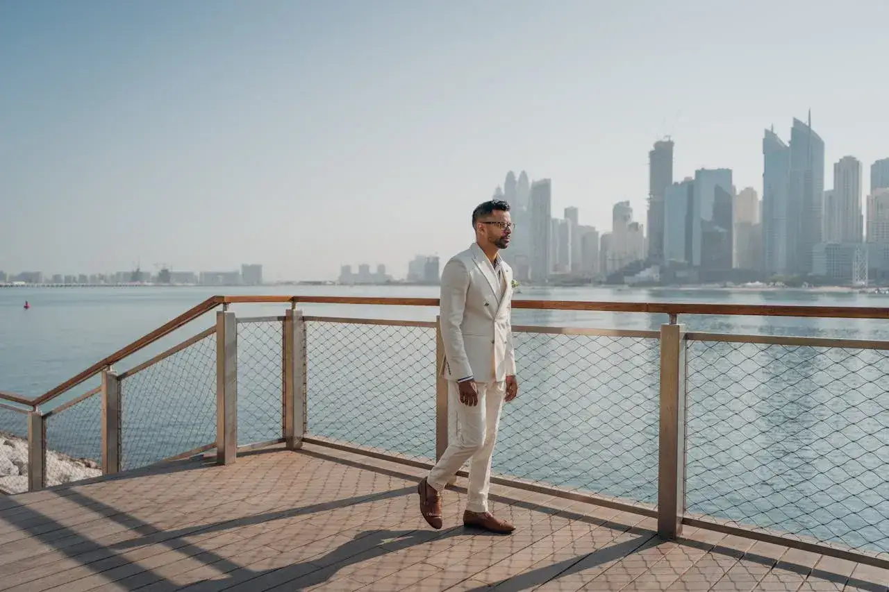 Elegancki mężczyzna w jasnym garniturze spaceruje nad wodą w Dubaju, myśląc o przyszłości i potencjalnym podatku w Dubaju.