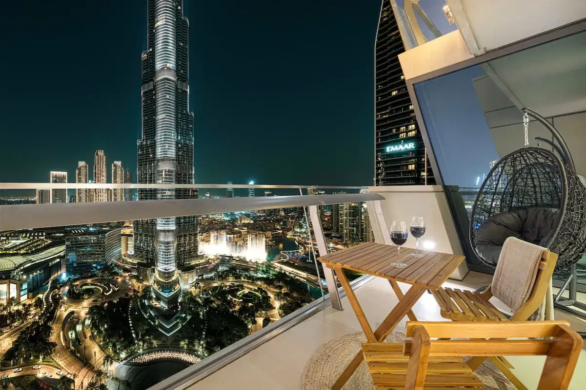 Luksusowe apartamenty w Dubaju z widokiem na nocne miasto i Burdż Chalifa. Na balkonie stolik z winem i wygodny fotel wiszący.